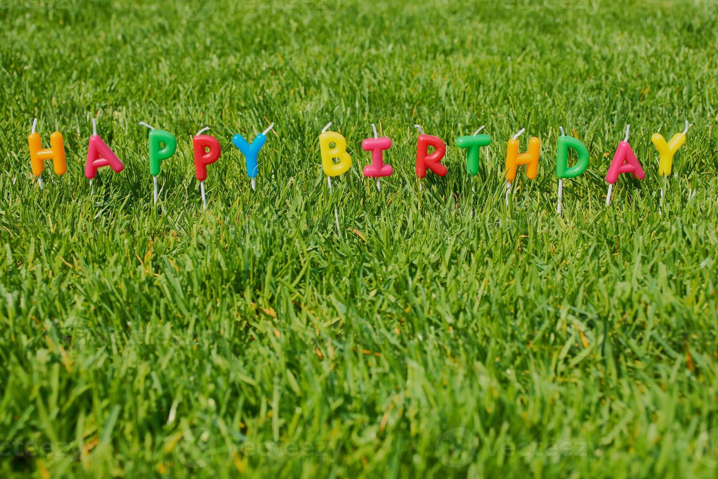 words happy birthday with colored candles on green grass photo