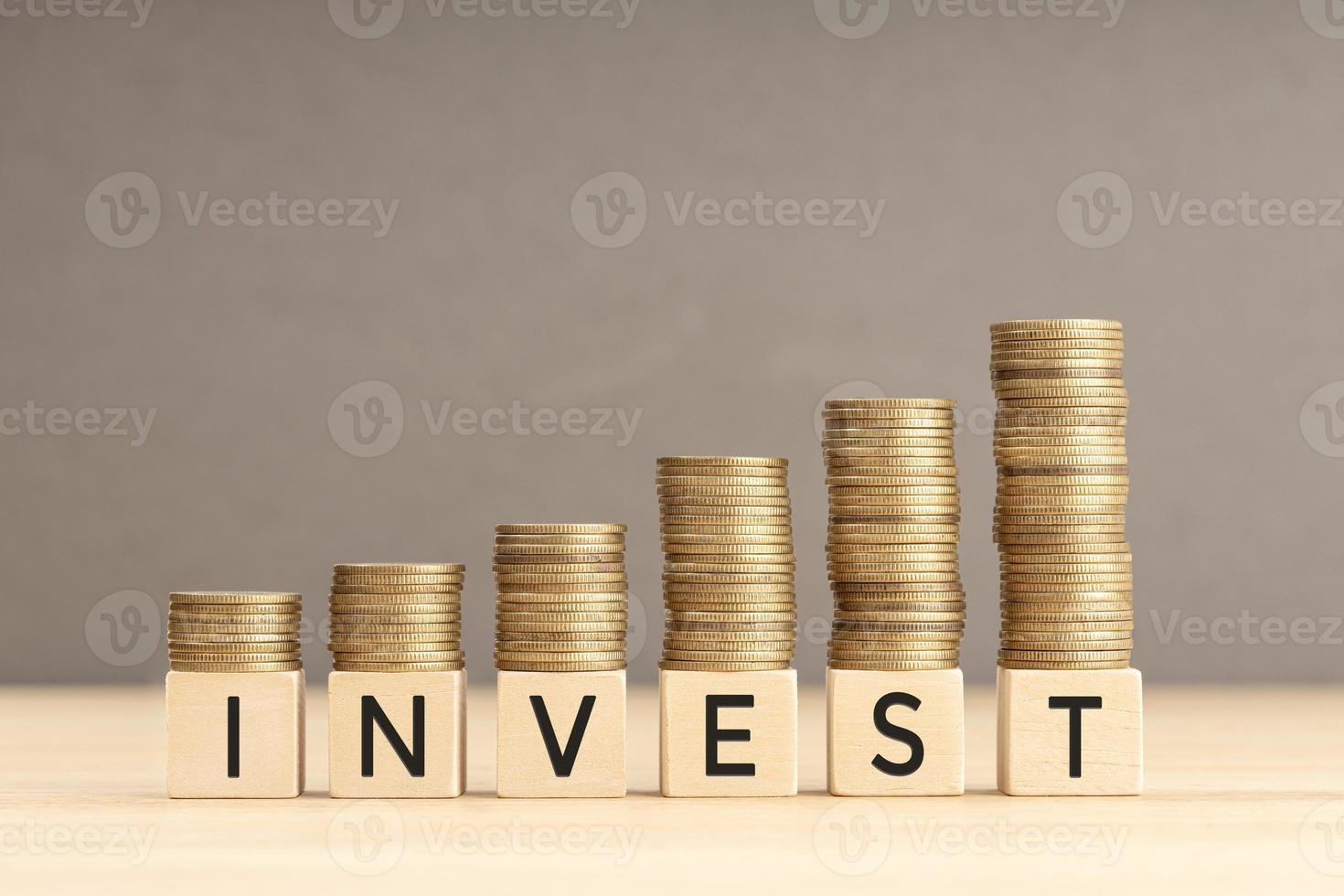 Invest word in wooden blocks with coins stacked in increasing stacks. Investing growing concept. Copy space photo