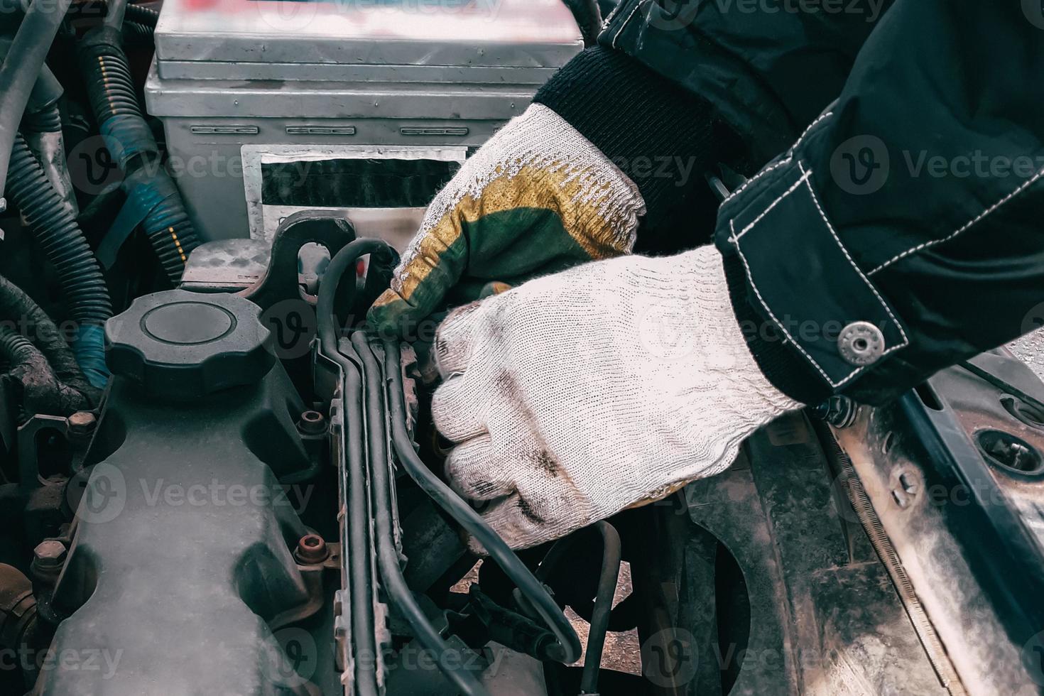 Auto mechanic repairs car engine. Man's hands in work gloves close-up. Diagnostics and restoration of old parts. Replacement of high-voltage wires. photo