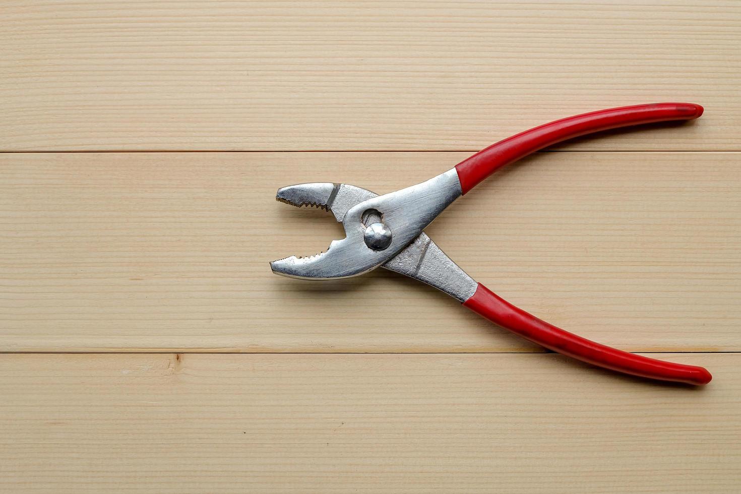 Top view and close up. Builder, repair and construction hand tool concept. There is red pliers on wooden table background. photo