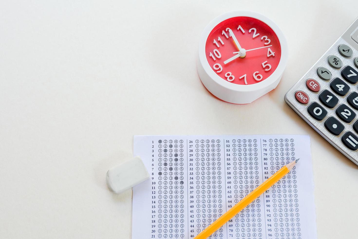 Answers sheet with green sharp pencil, clock, calculator and rubber isolated on white background. Top view of them. Take the exam timely concept. photo