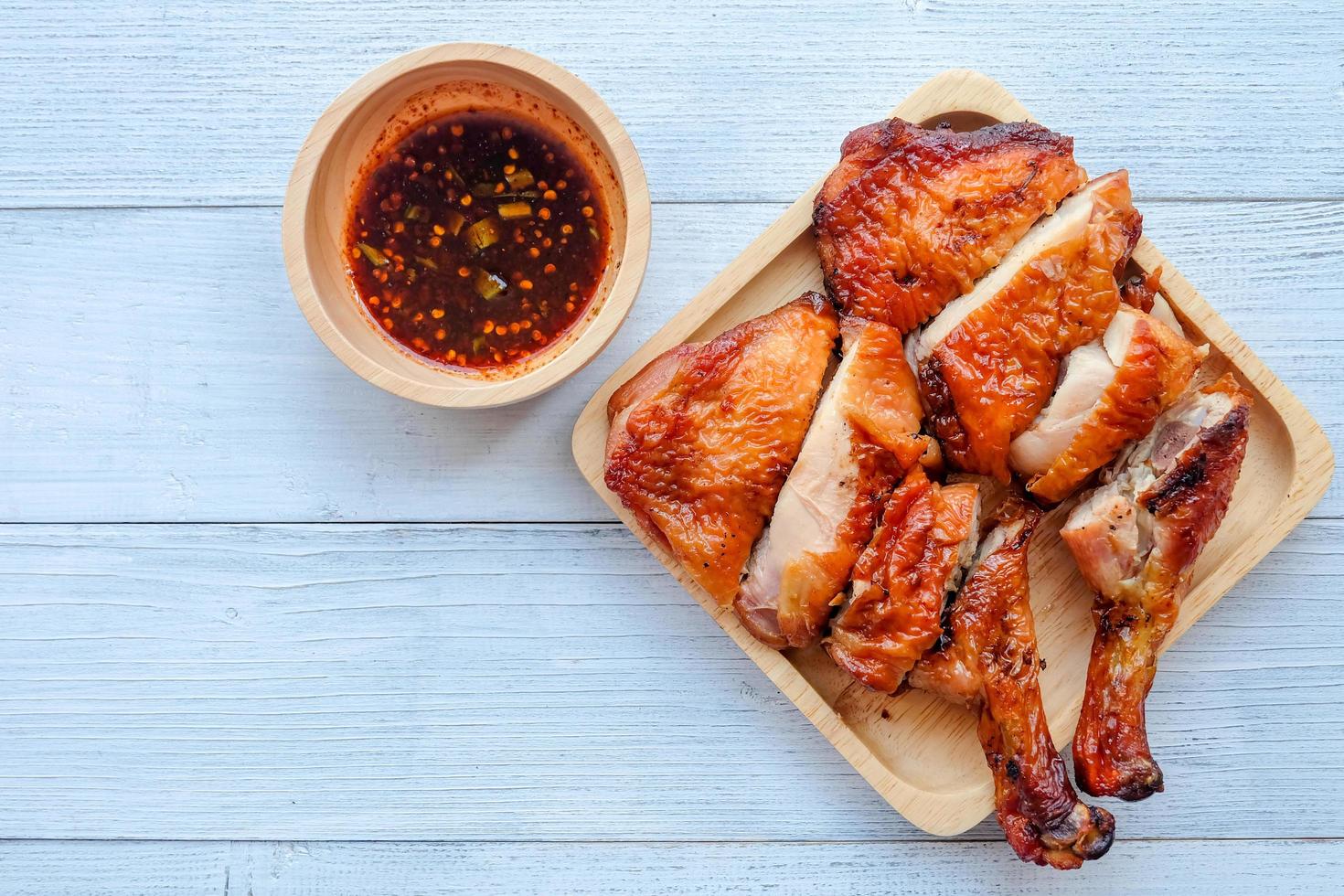 Top view and close up of juicy grilled chicken wing on wooden plate and spicy Thai Style sauce on white vintage wooden background. Recommend menu with papaya salad famous and popular food. photo