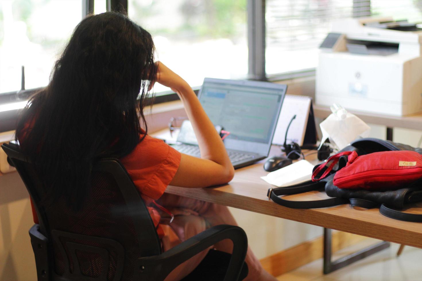 A young woman is sitting in an office seen from behind holding her head while doing her work photo