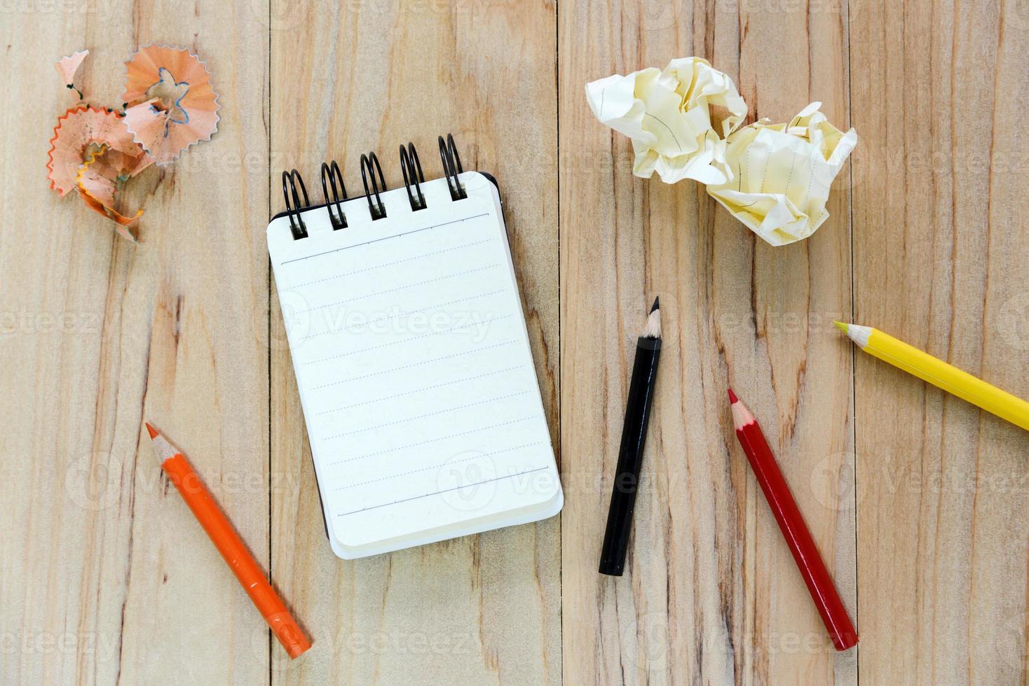 Small note book paper or notepad for writing information with color pencil and crumpled paper balls on wooden table. view from above photo