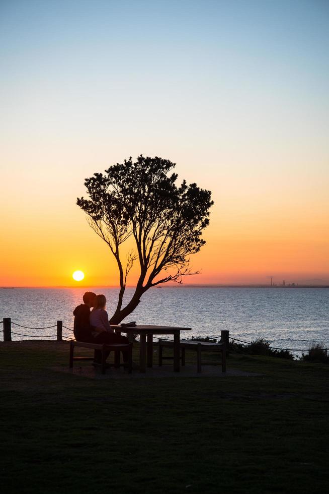 Romantic scene with couple sitting together and looking to beautiful sunset at Brighton beach, Australia. photo