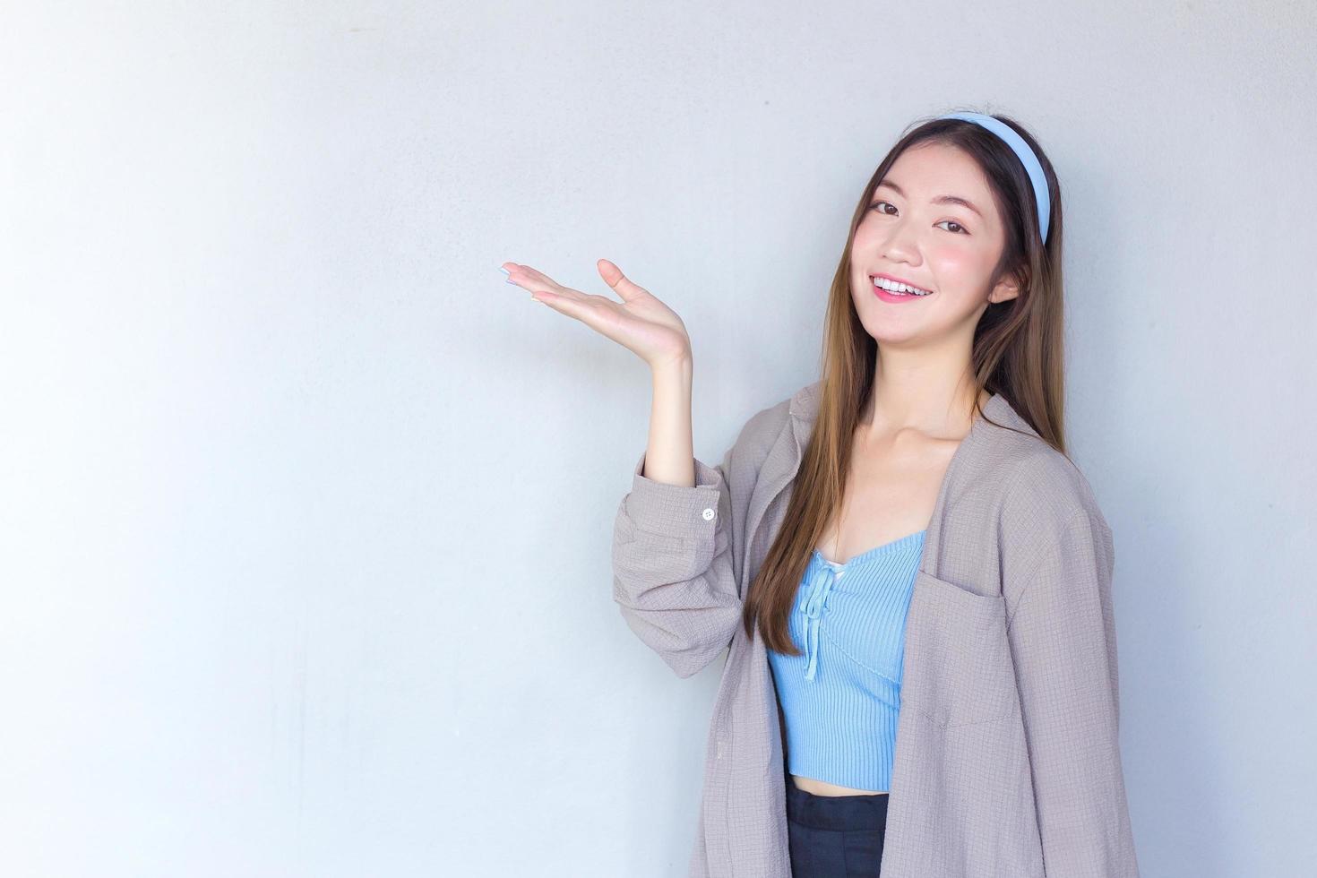 Beautiful young Asian woman long brown hair in a blue shirt is acting hand shows as presenting something on the background. photo