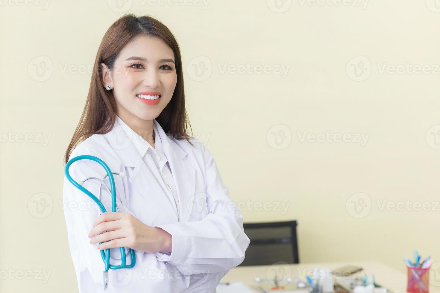 Young beautiful  Asian woman doctor Standing with arms crossed happy and smile in hospital. Wearing a white robe and stethoscope photo