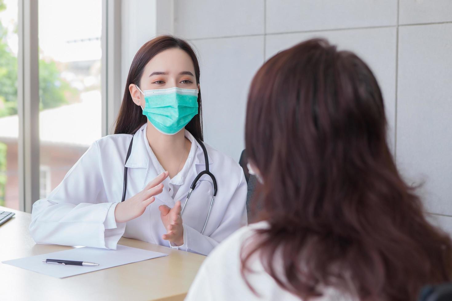 una doctora profesional asiática examina atentamente con una paciente anciana sobre sus síntomas mientras ambas usan máscaras médicas para prevenir infecciones en la sala de examen del hospital. foto