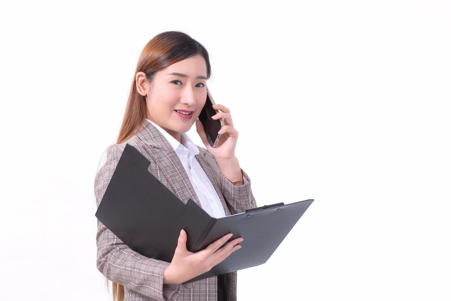 Asian working woman in formal suit with white shirt is calling telephone and opens document file or clipboard to check data on white background. photo