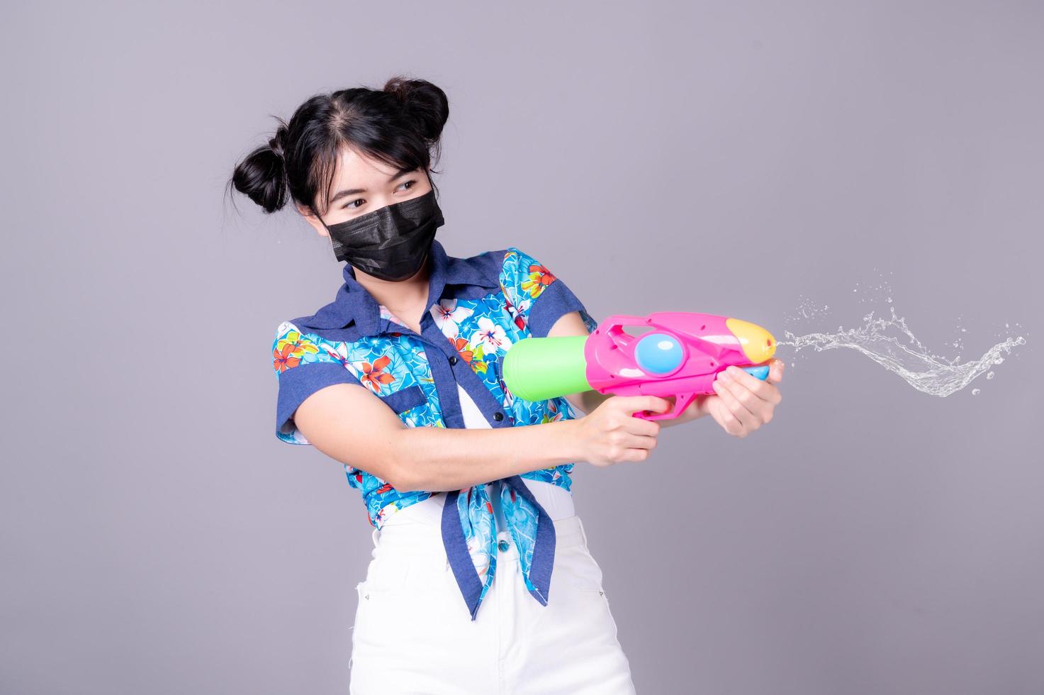 Beautiful Asian women wear a surgical mask while holding a plastic water gun during Songkran festival photo