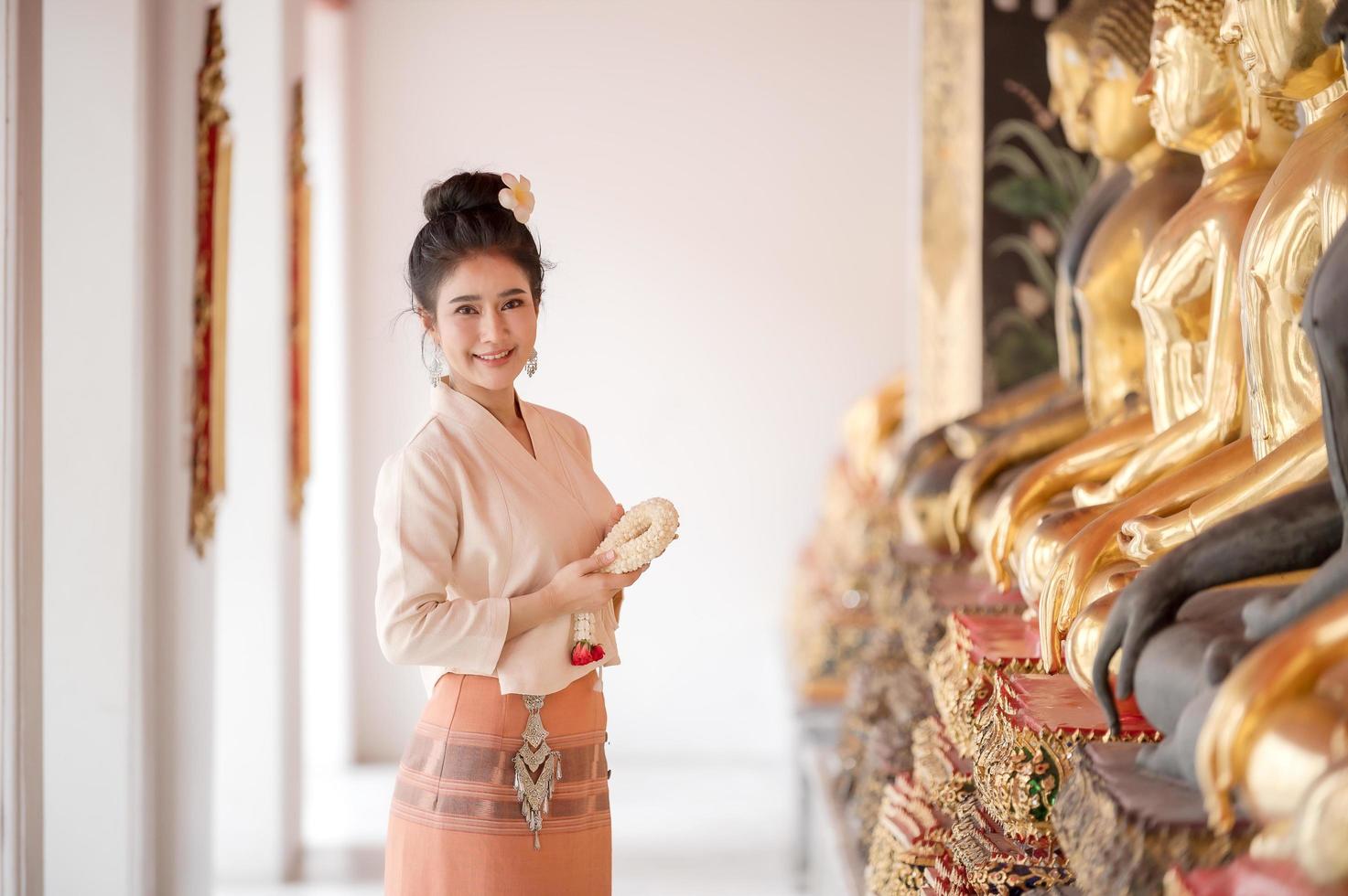 atractiva mujer tailandesa con un antiguo vestido tailandés sostiene una guirnalda de flores frescas que rinden homenaje a buda para pedir un deseo en el festival tradicional de songkran en tailandia foto