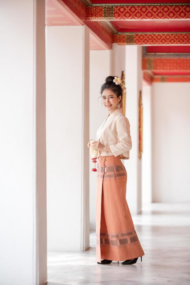 atractiva mujer tailandesa con un antiguo vestido tailandés sostiene una guirnalda de flores frescas que rinden homenaje a buda para pedir un deseo en el festival tradicional de songkran en tailandia foto