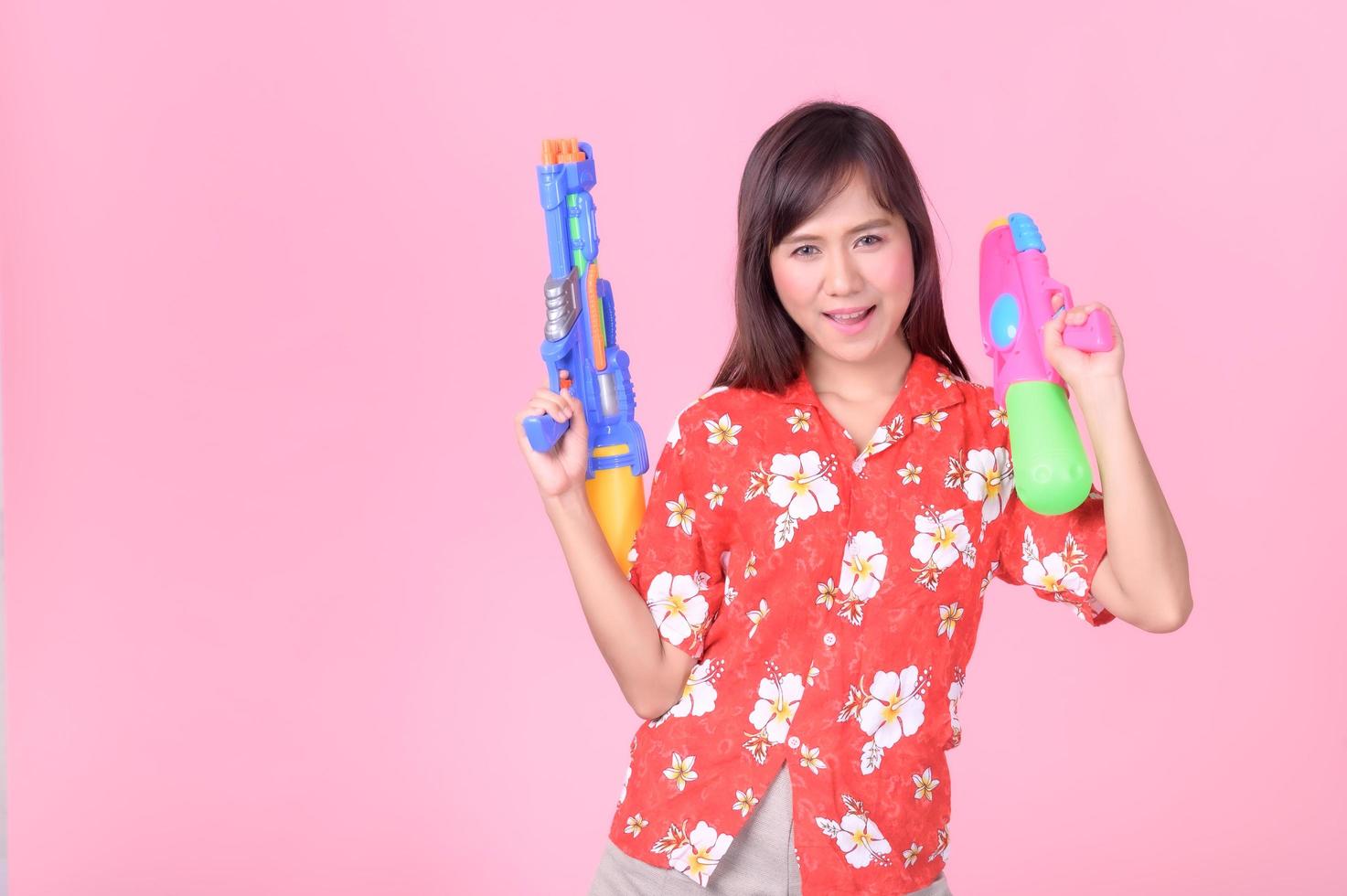 A beautiful Asian woman shows a gesture while holding a plastic water gun during the Songkran festival photo