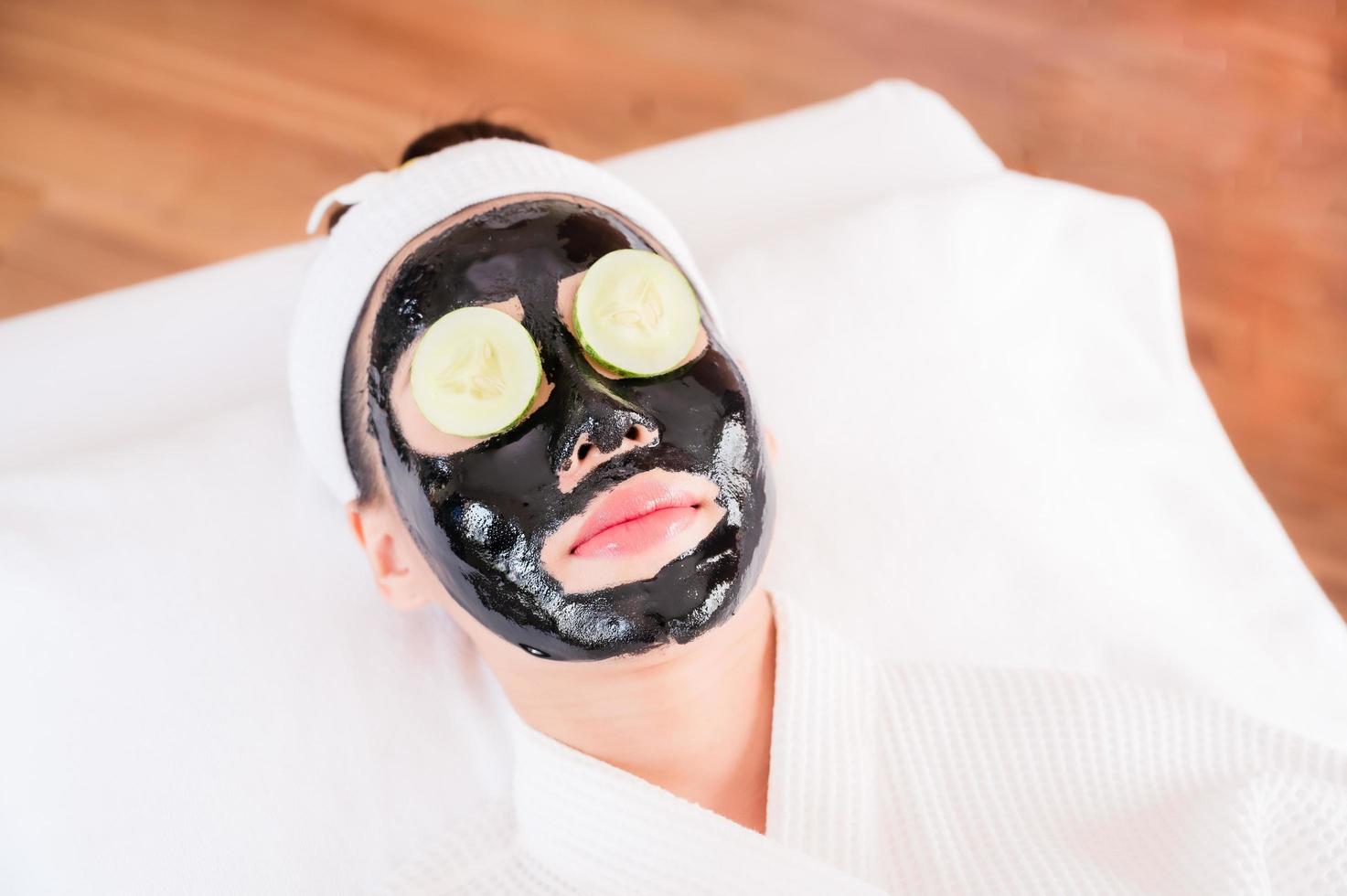 A beautiful Asian woman uses spa mud and cucumber for facial treatment photo