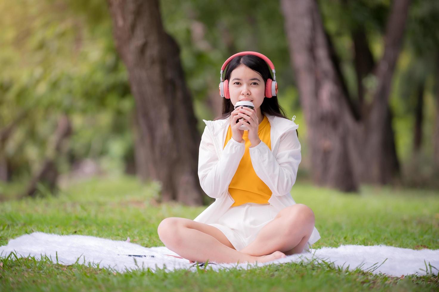 A beautiful Asian woman relaxing in the garden by drinking hot coffee and listening to internet music online photo