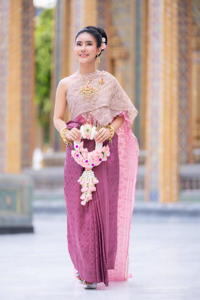 A beautiful elegant Thai woman in Thai dress adorned with precious jewelry stands holding a flower garland photo