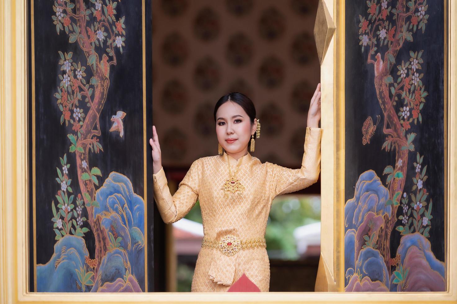 A beautiful, graceful Thai woman in Thai dress adorned with valuable jewelry stands in a beautiful ancient Thai temple photo