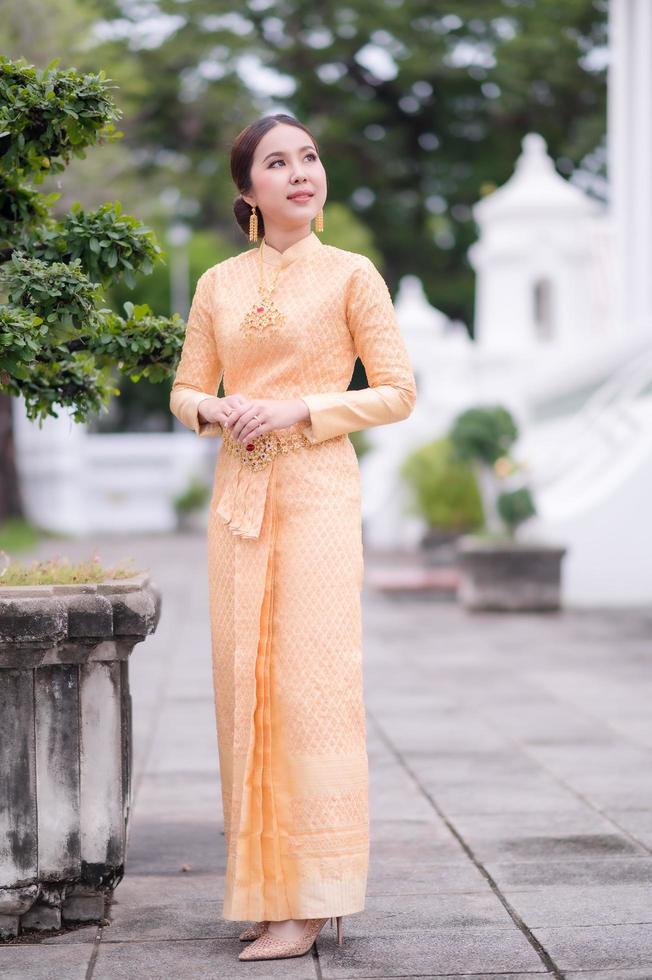 A beautiful, graceful Thai woman in Thai dress adorned with valuable jewelry stands in a beautiful ancient Thai temple photo