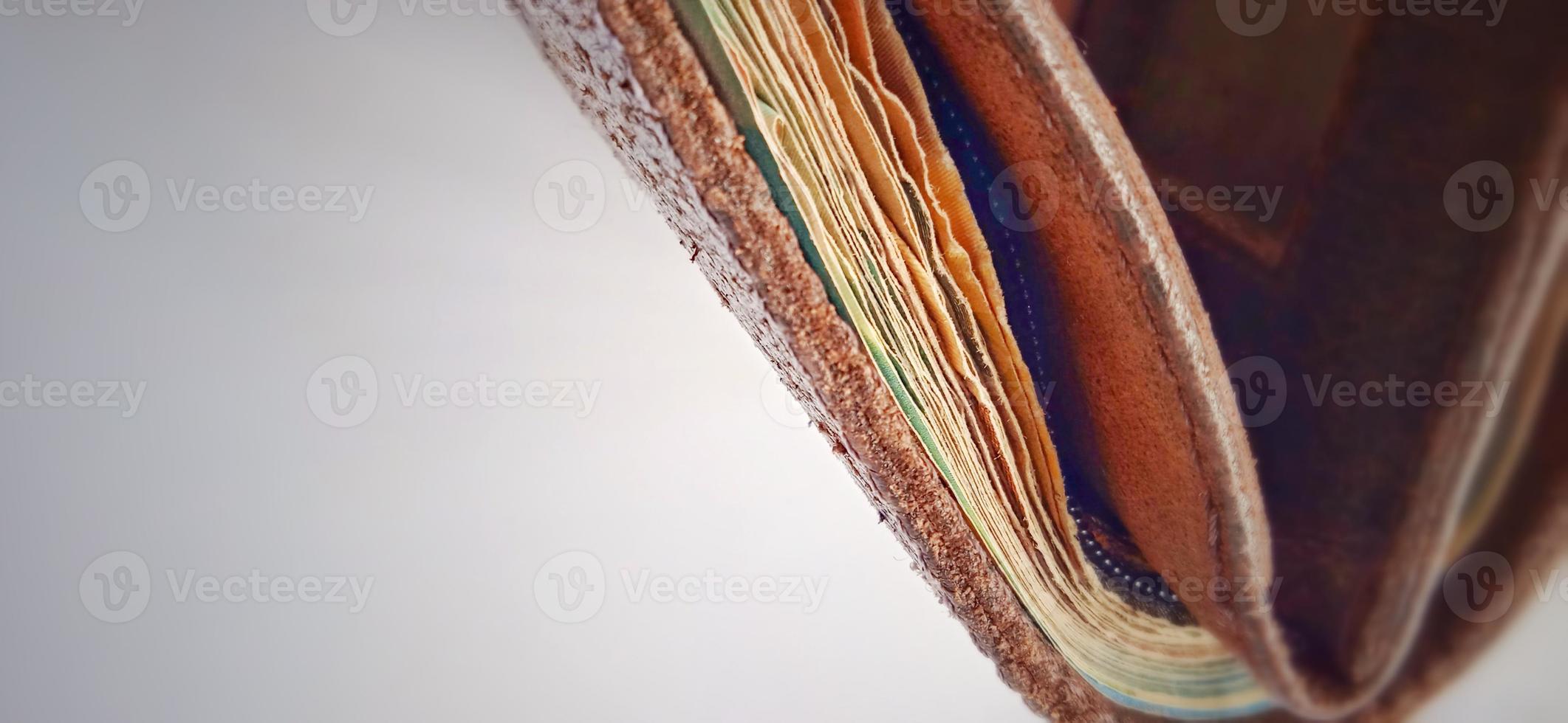 An old brown orange synthetic wallet with some money inside on the dim grey yellow background. photo