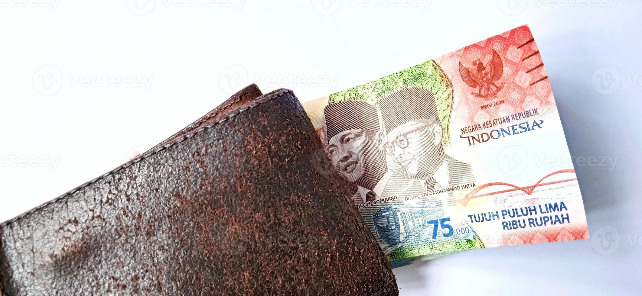 Santuario escribir barco un billete de 75.000 rupias del banco indonesia bajo la cartera naranja  oscuro con fondo gris.