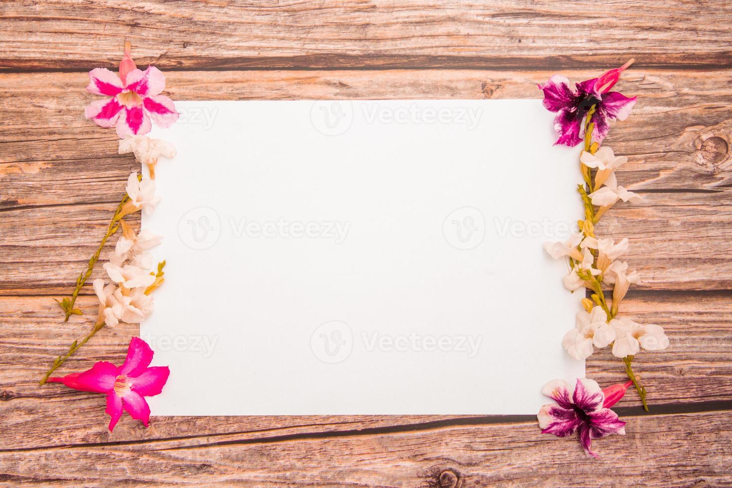 Pink azalea flowers with white asystasia gangetica flowers and blank paper sheet on a wooden background.spring border pink and white blossom, top view, Blank template for your text. flat lay. photo