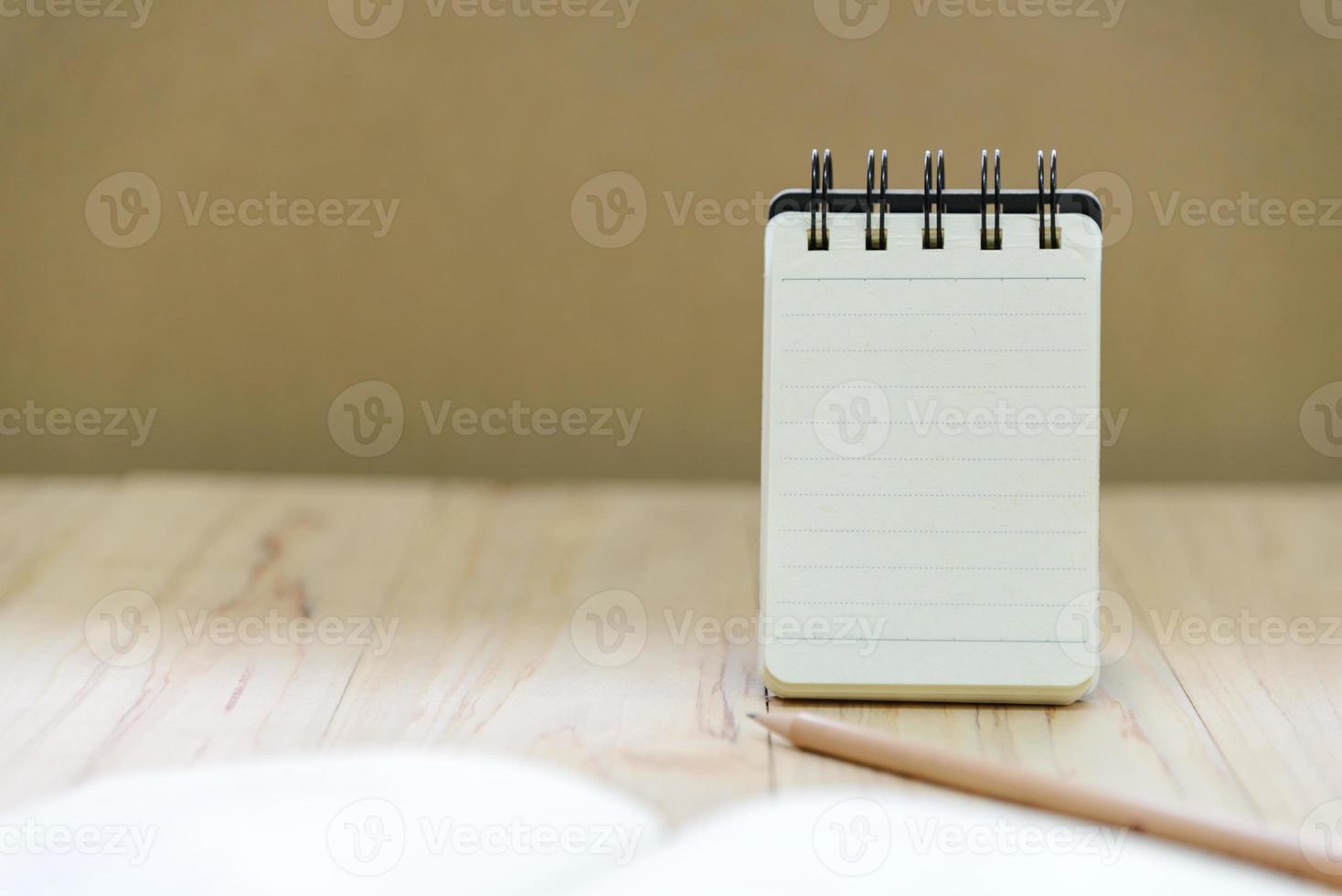 papel de cuaderno pequeño o soporte de bloc de notas para escribir información con lápiz y libro sobre mesa de madera foto