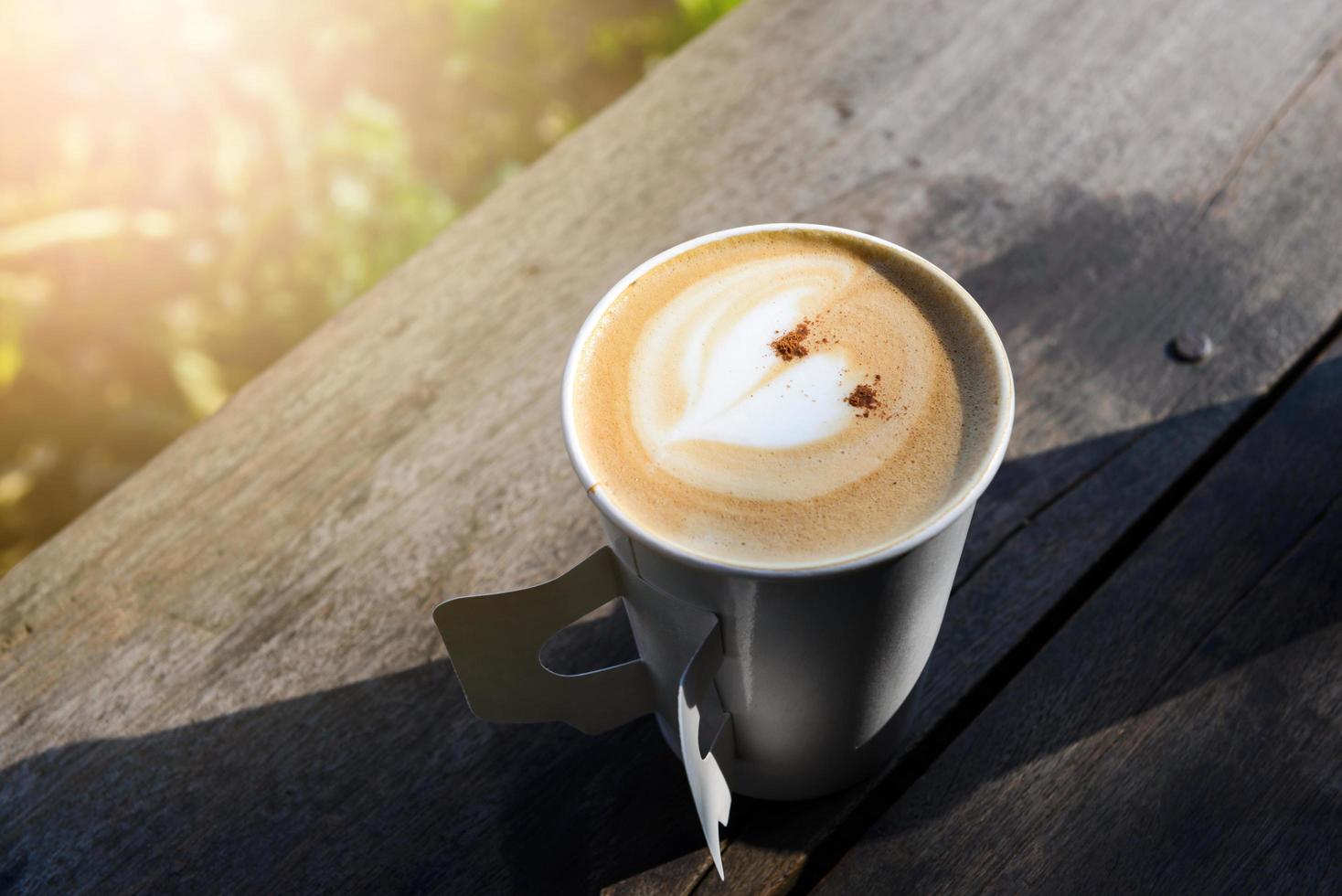 Paper cup of coffee on wooden table at the garden, copy space background photo