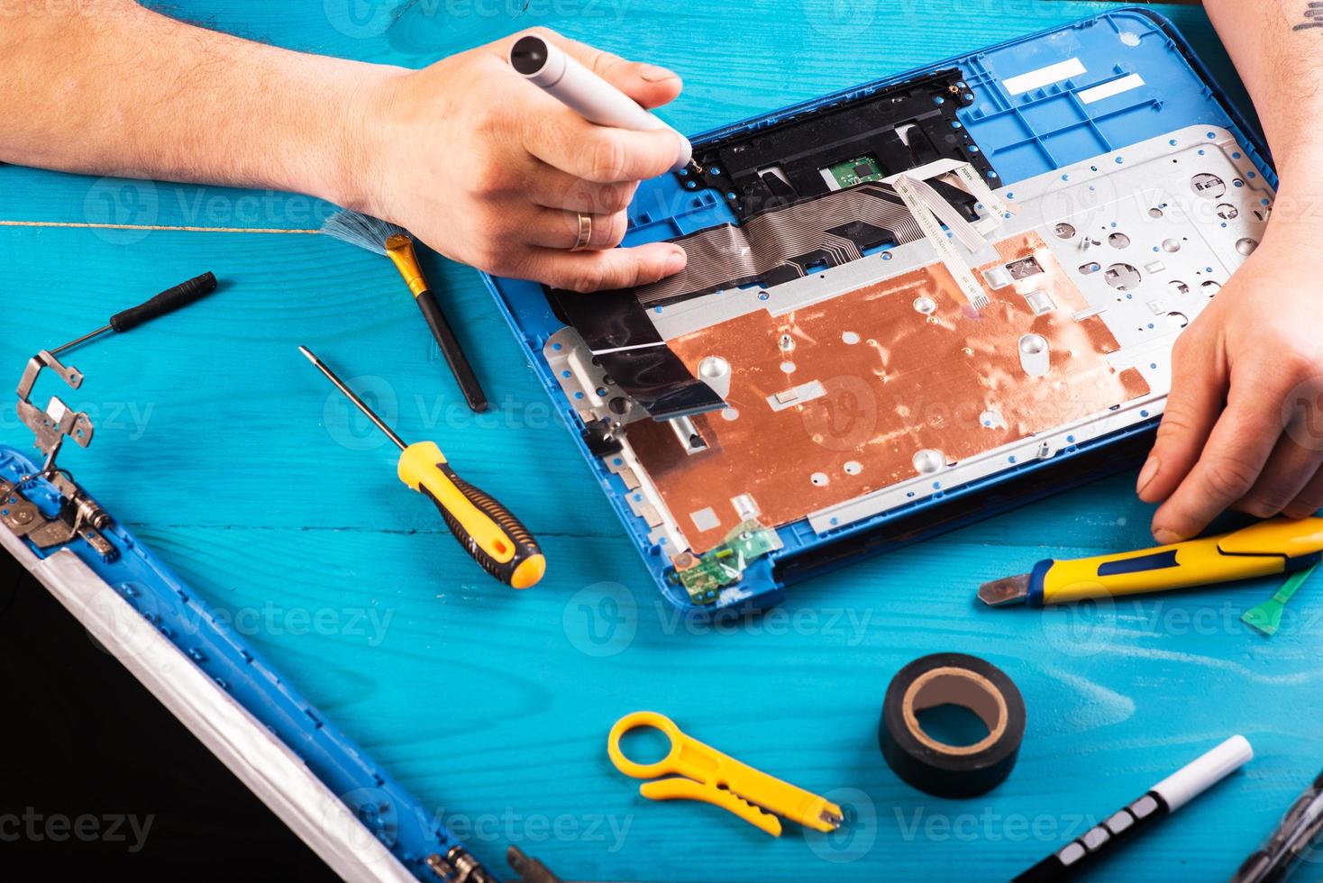 Wizard repairs laptop with tools and hands on the blue wooding table. top view photo