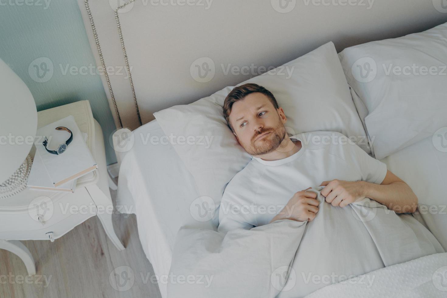 Handsome stressed young caucasian male lying in bed with his eyes open photo