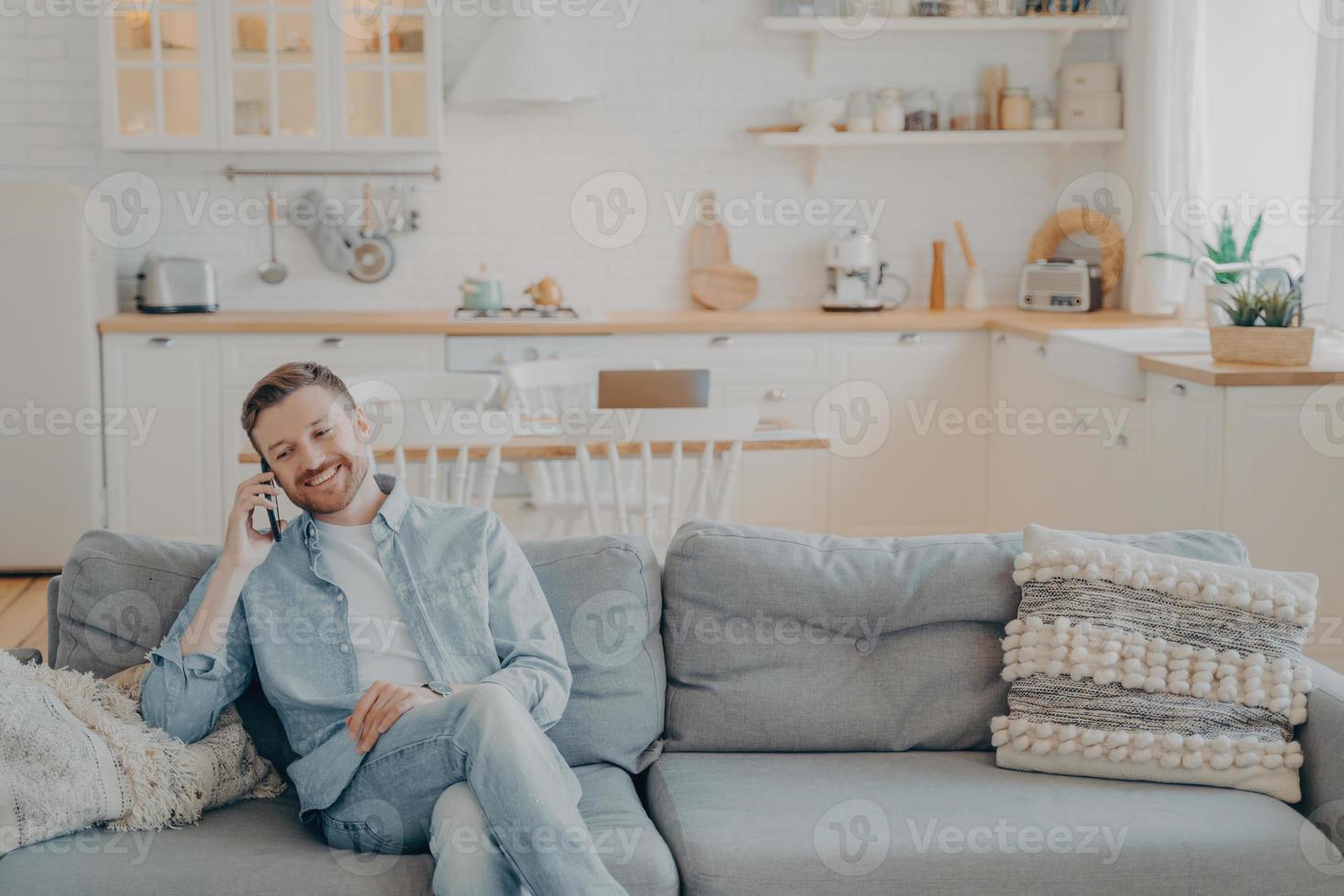 Young man talking on phone with his friend while sitting on couch photo