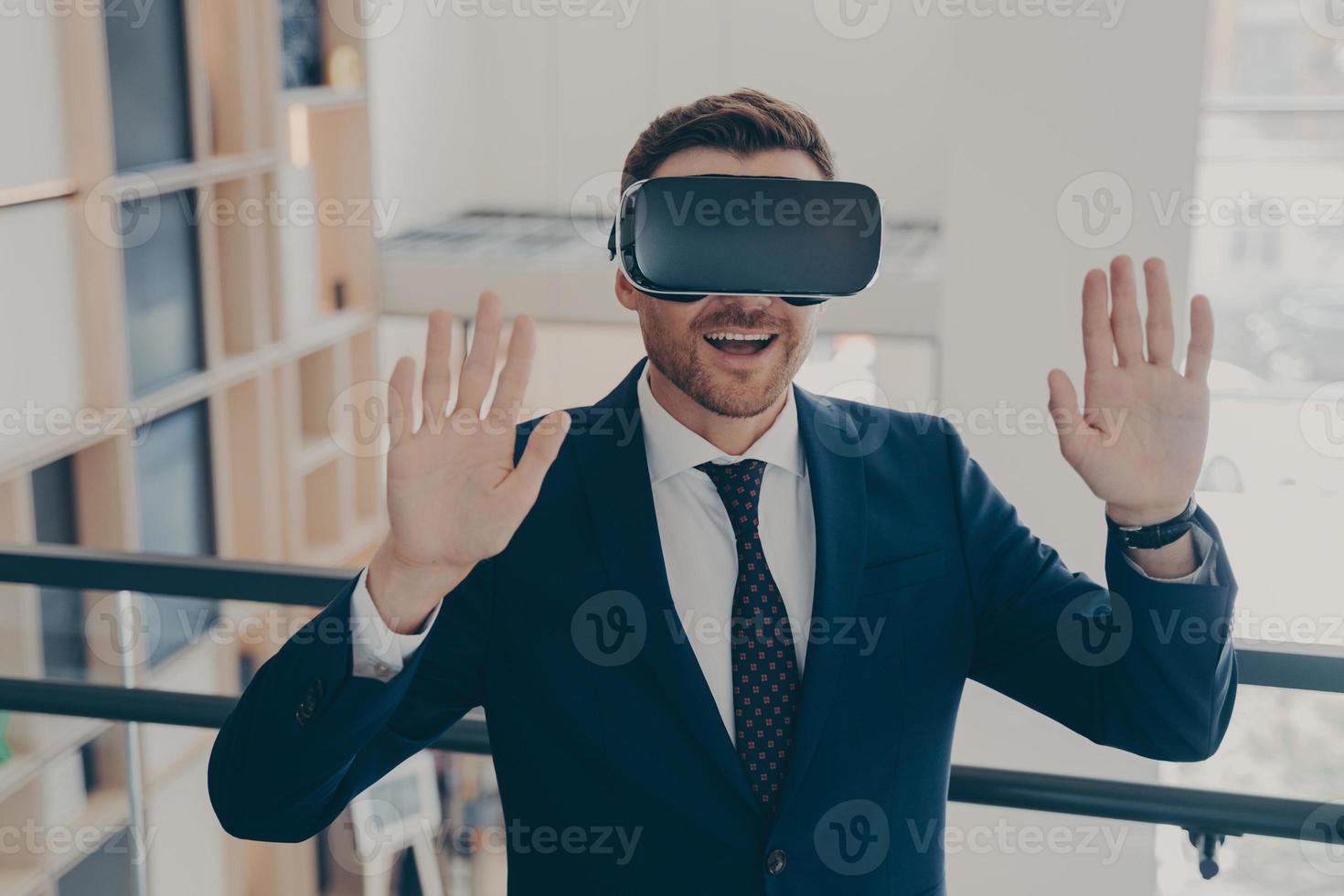 Smiling office worker in suit in 3d goggles enjoying cyberpace experience with raised arms photo