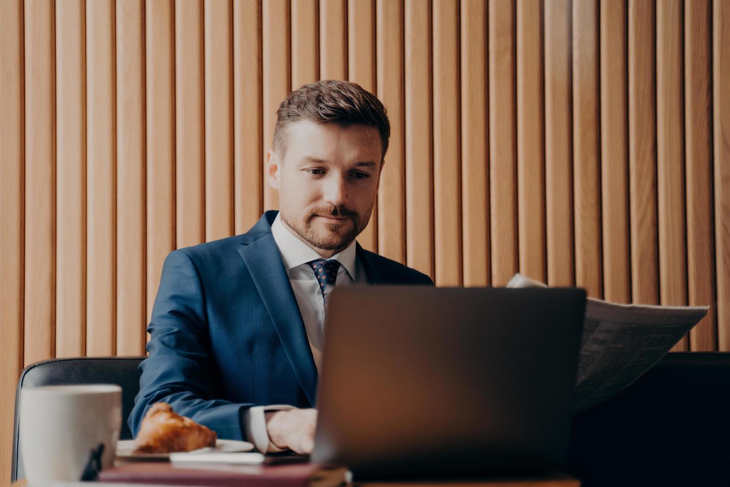 Portrait of handsome elegant financier in suit working on laptop in cafe photo