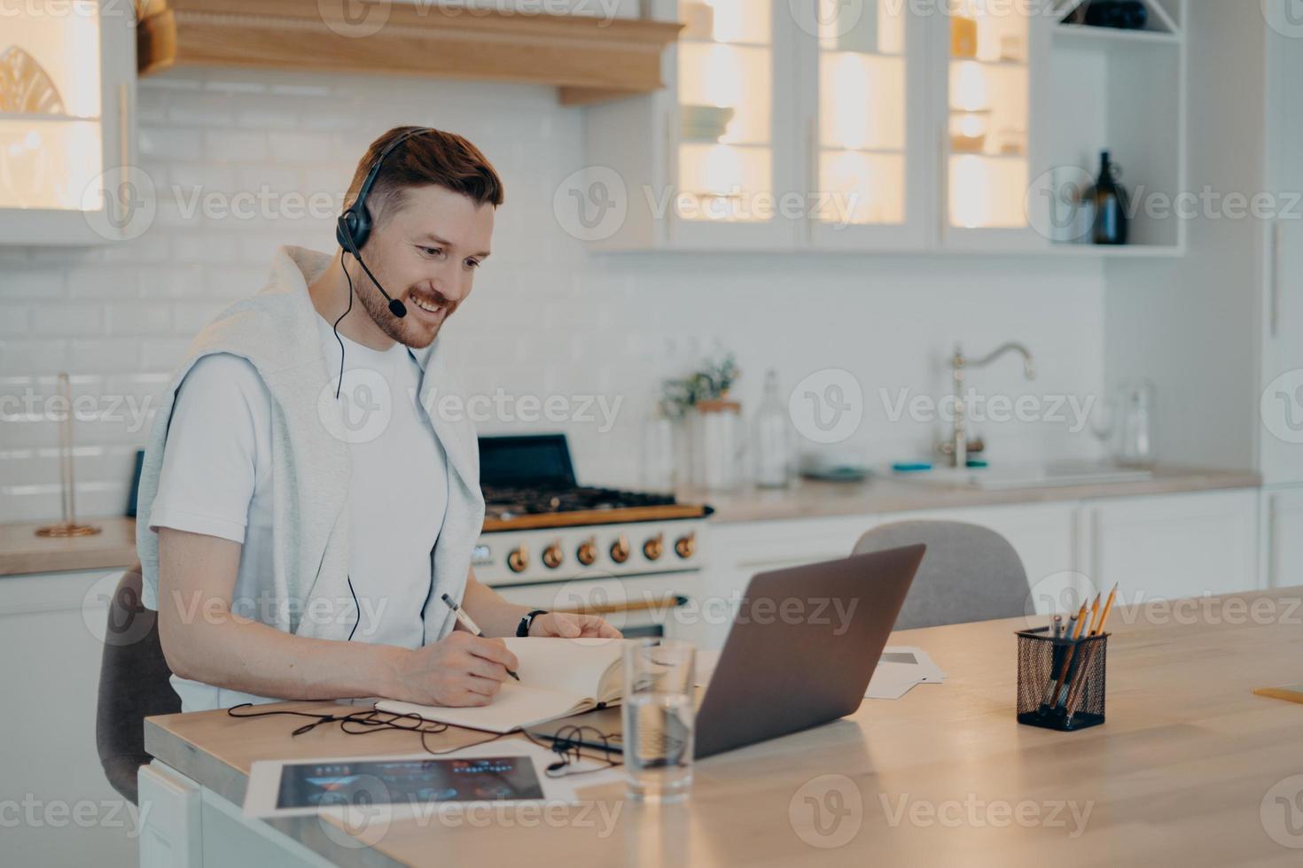 joven feliz tomando notas en un cuaderno durante una videollamada foto