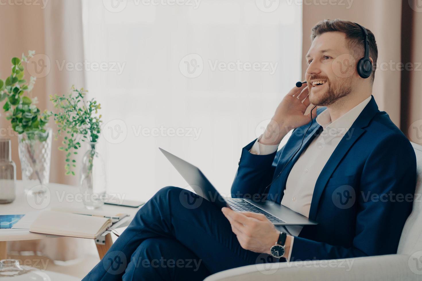 hombre de negocios barbudo sonriente hablando con su colega en los auriculares en casa foto