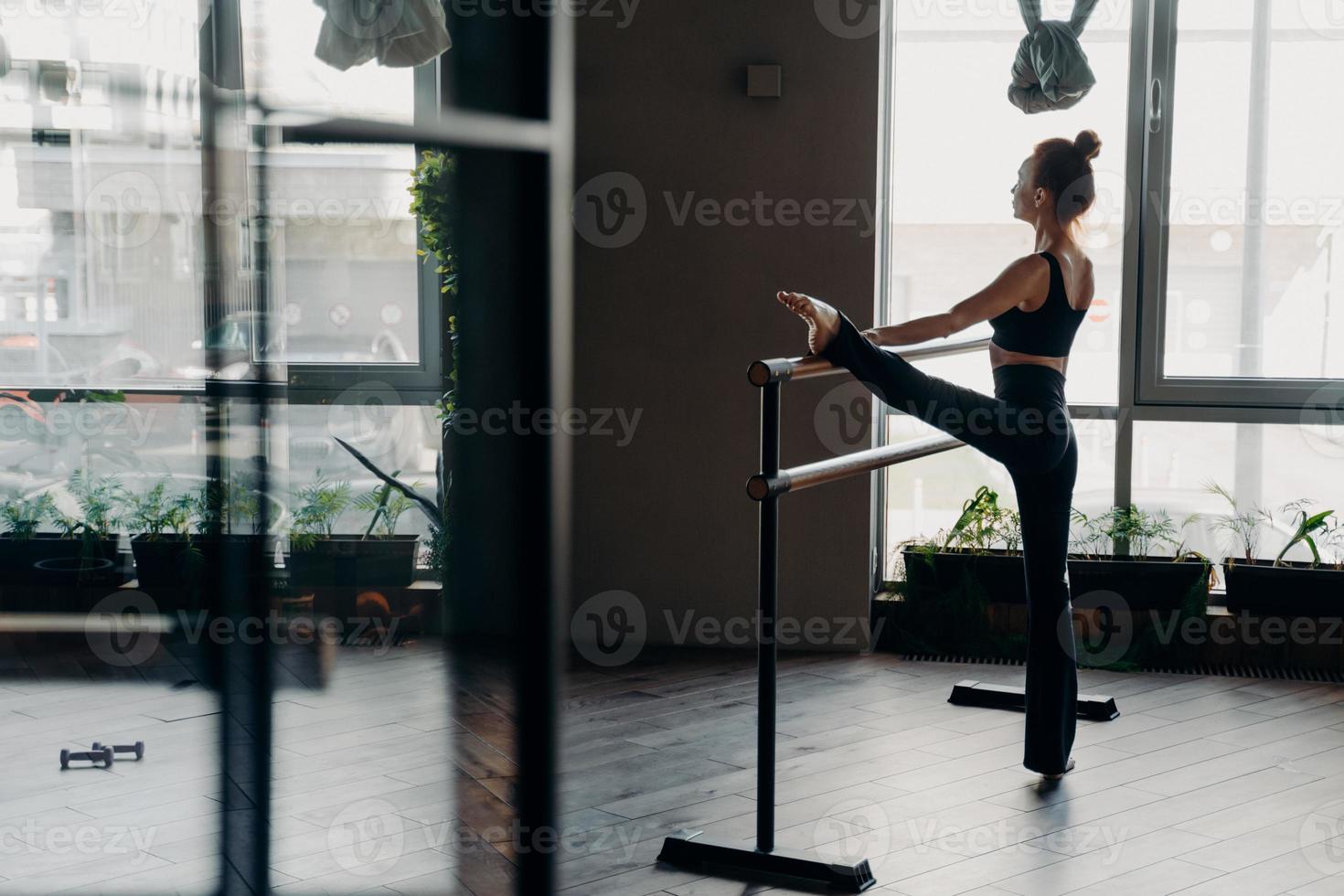 Slim ballerina during her stretch routine next on ballet barre in studio photo