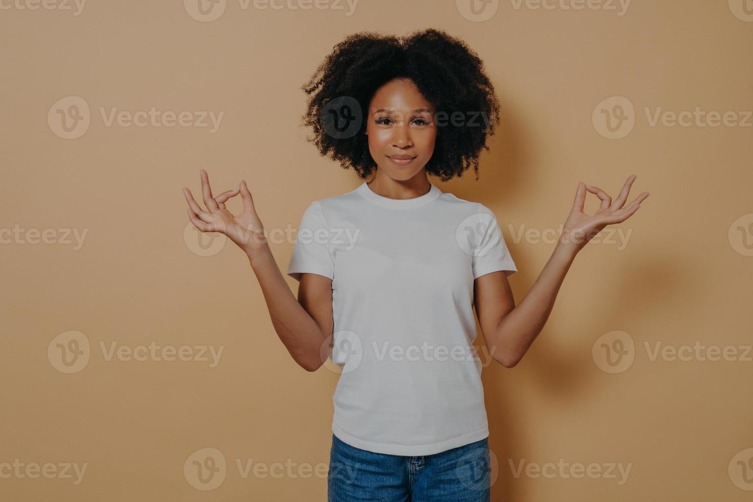 Peaceful afro american young woman keeping hands in mudra gesture, isolated on beige wall photo