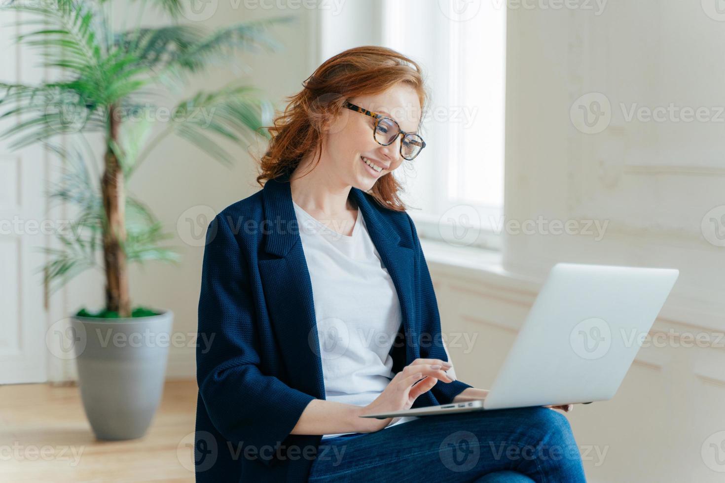 Sideways shot of financial expert prepares report on notebook, keyboards information on laptop computer, browses information on laptop computer, dressed in formal wear, develops startup project photo