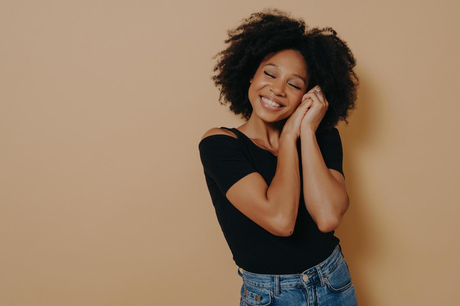 Cute woman keeping hands near face and dreaming of something good, isolated over beige wall photo