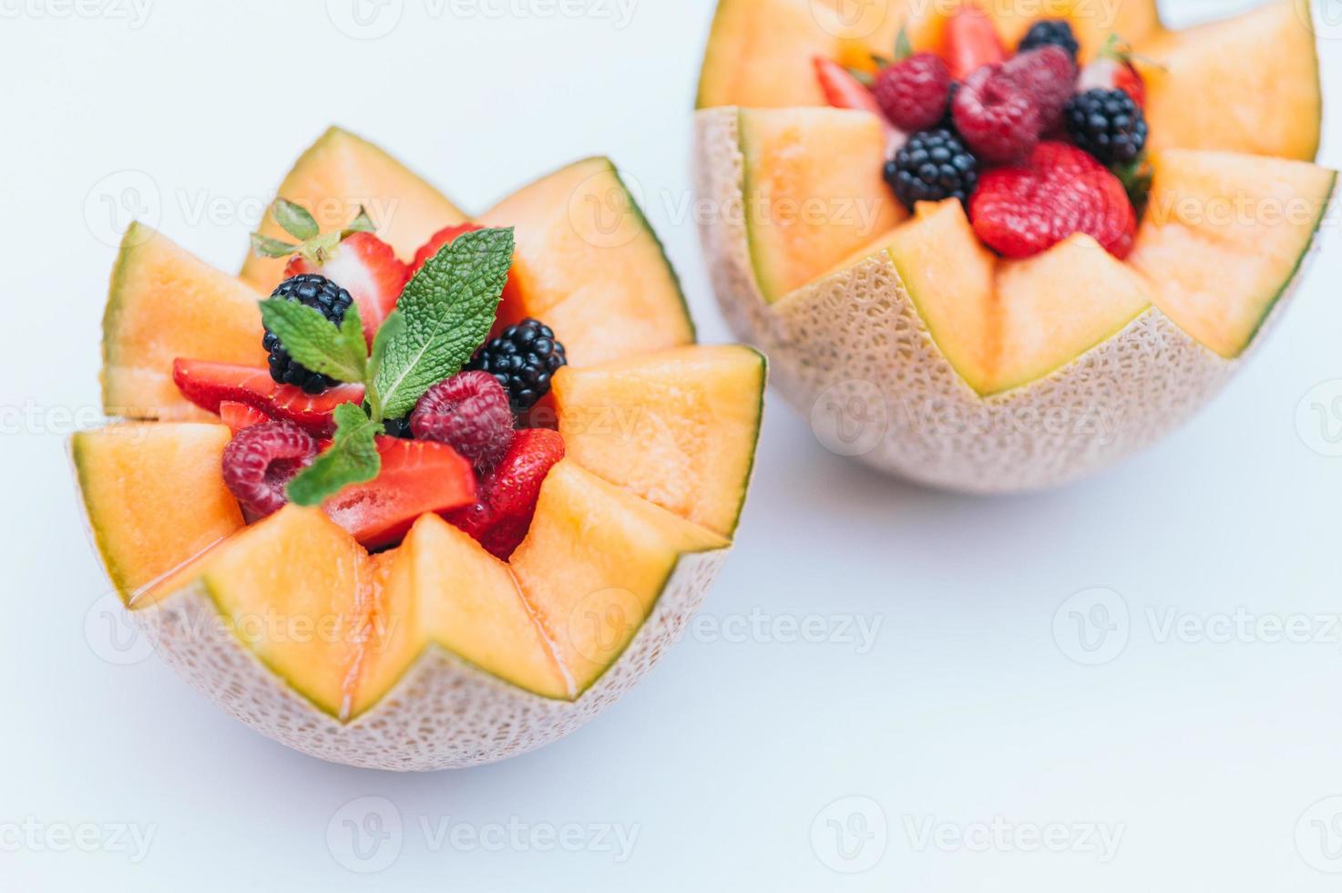 Food design and healthy nutrition concept. Delisious fresh raspberry, strawberry and blackberry with mint in carved melon. Cantaloupe with fruit against white background. photo