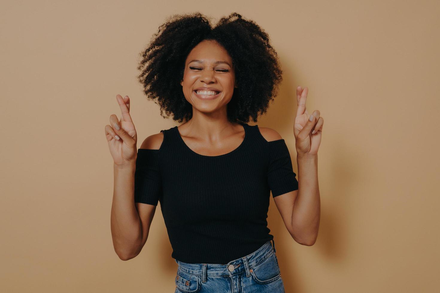 linda y encantadora mujer afroamericana posando con ropa informal mientras gesticulaba con los dedos cruzados foto