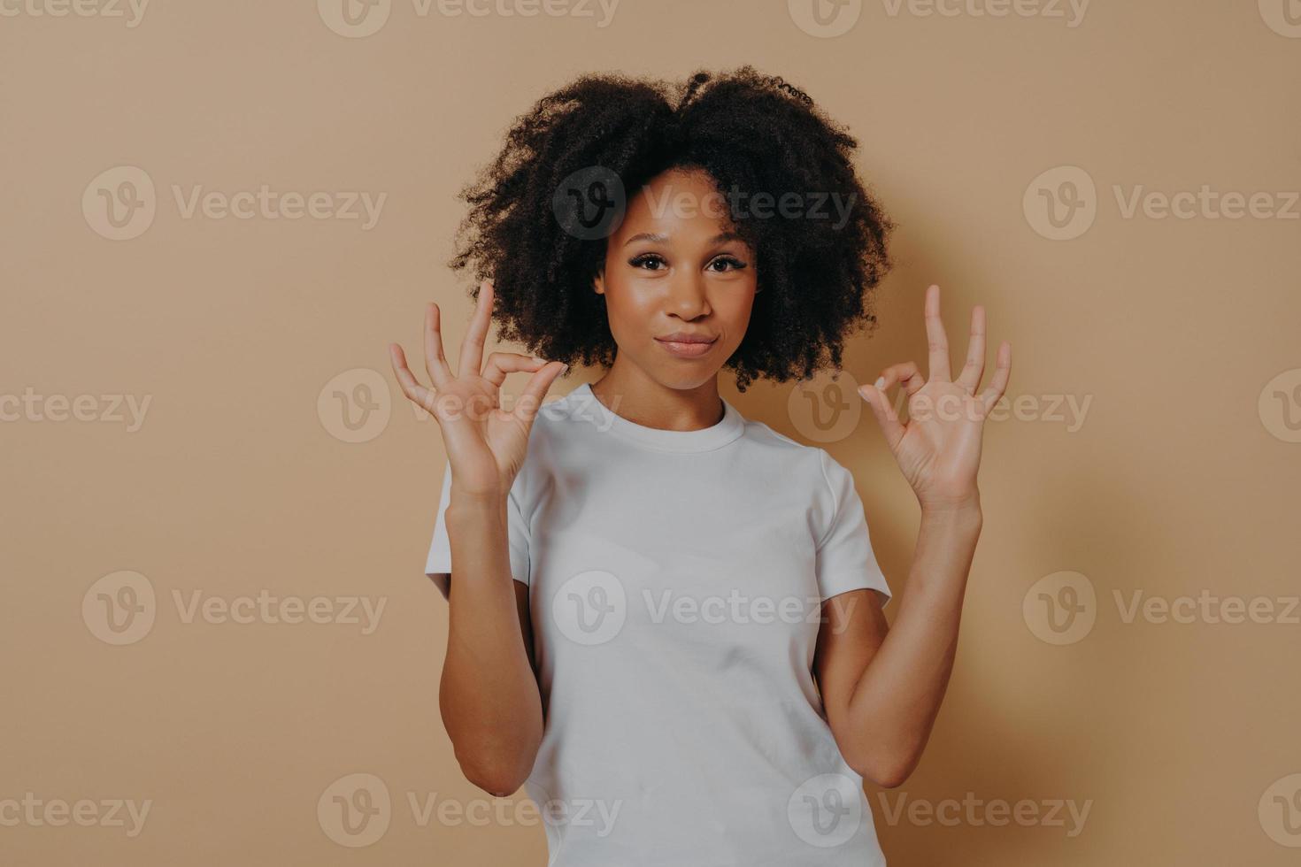 Young african american lady keeping both hands in okay gesture, isolated over brown background photo