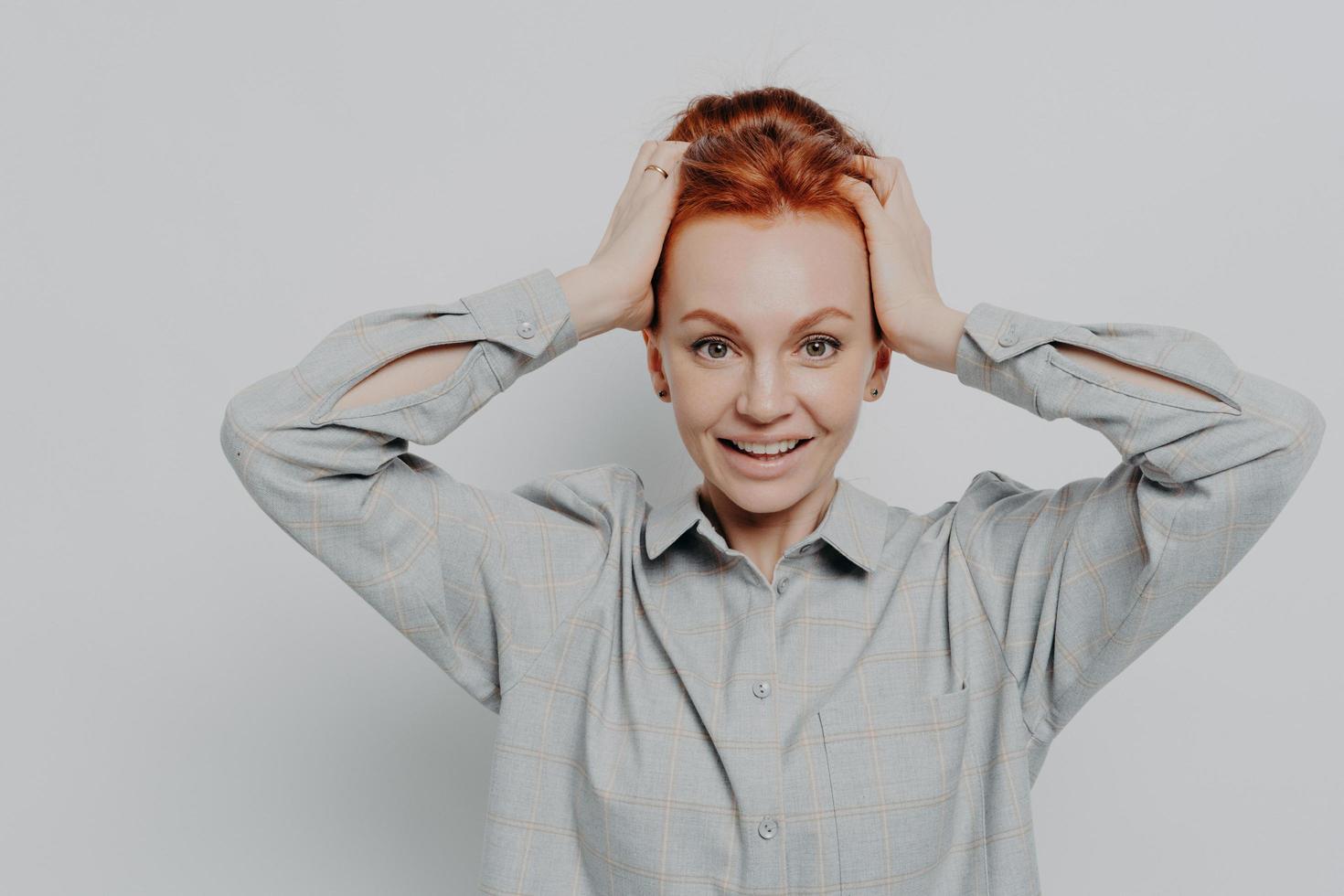 Excited amazed redhaired woman holding head in hands and looking at camera with surprised expression photo