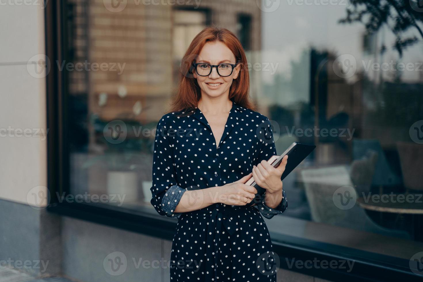 Redhead businesswoman walks in urban place holds tablet and diary photo