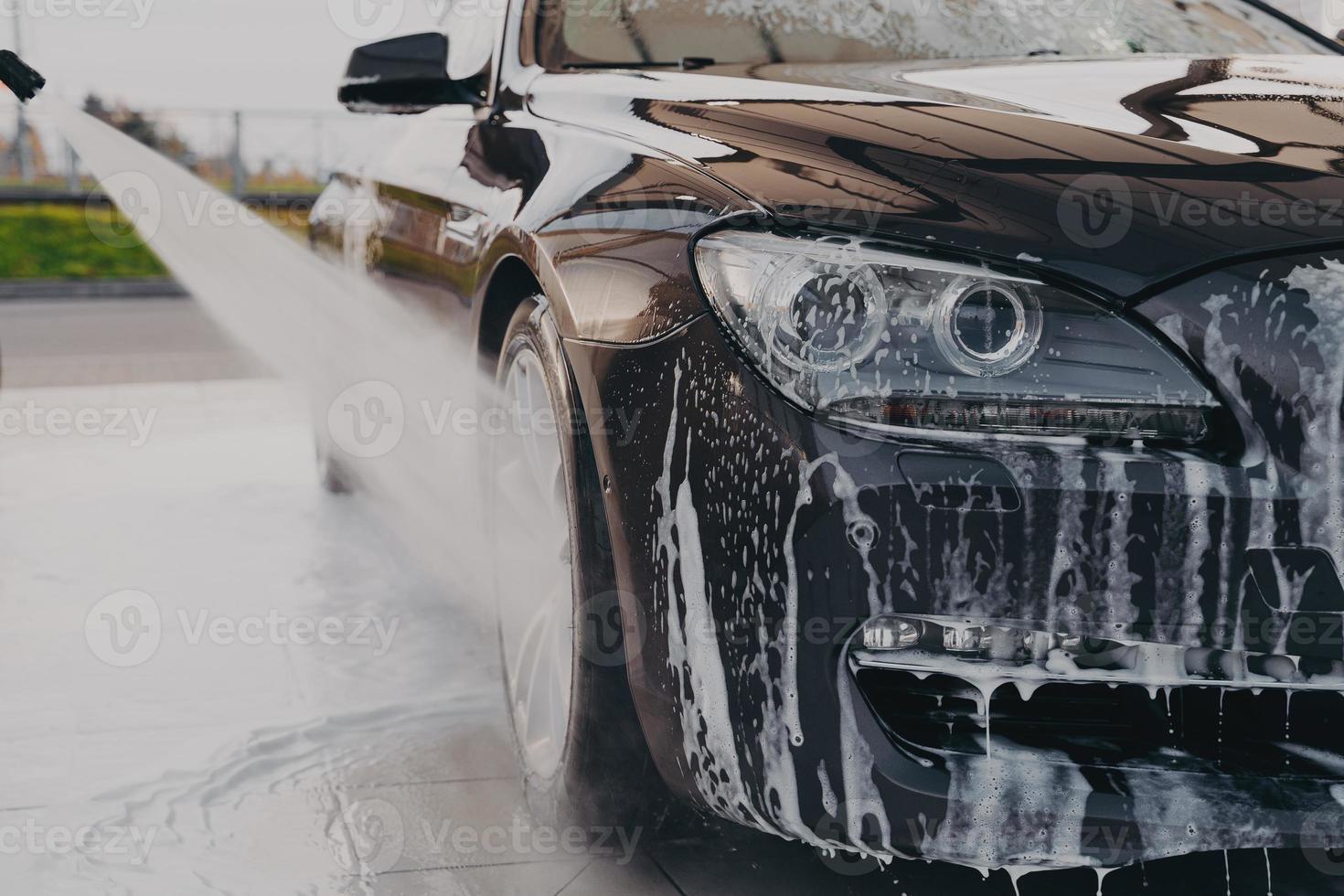 Professional car wash, spraying water from high pressure washer to rinse off suds photo