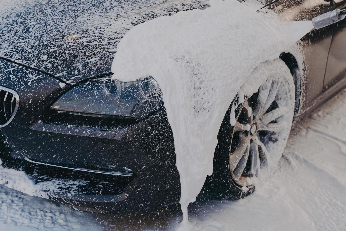 coche negro en espuma de jabón blanco en la estación de lavado foto