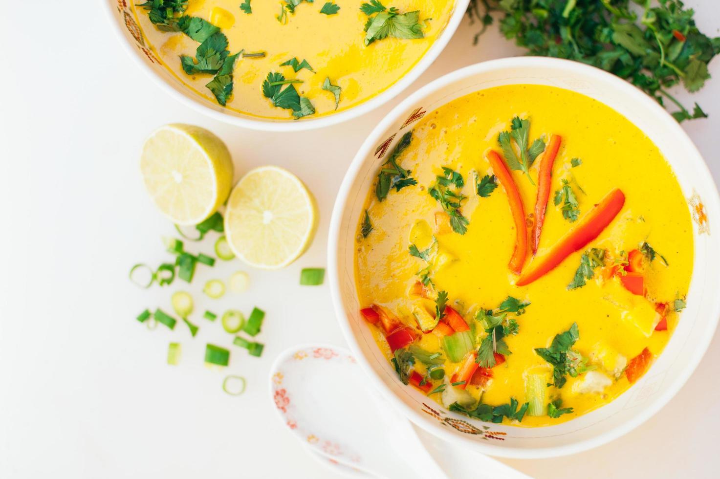 Bowl of fresh curry soup with red bell pepper, parsley against white background. Fresh vegetable dish. Two slices on lime near bowls of soup. Top view photo