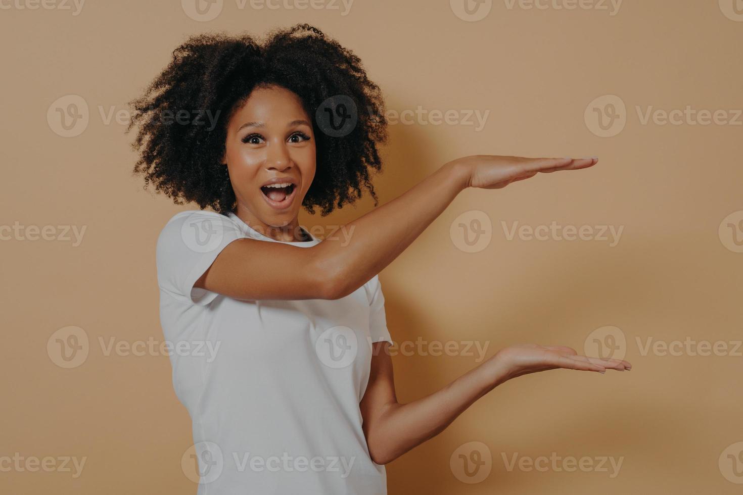 Exited Afro American beautiful young woman with black curly hair showing with hands example of size photo