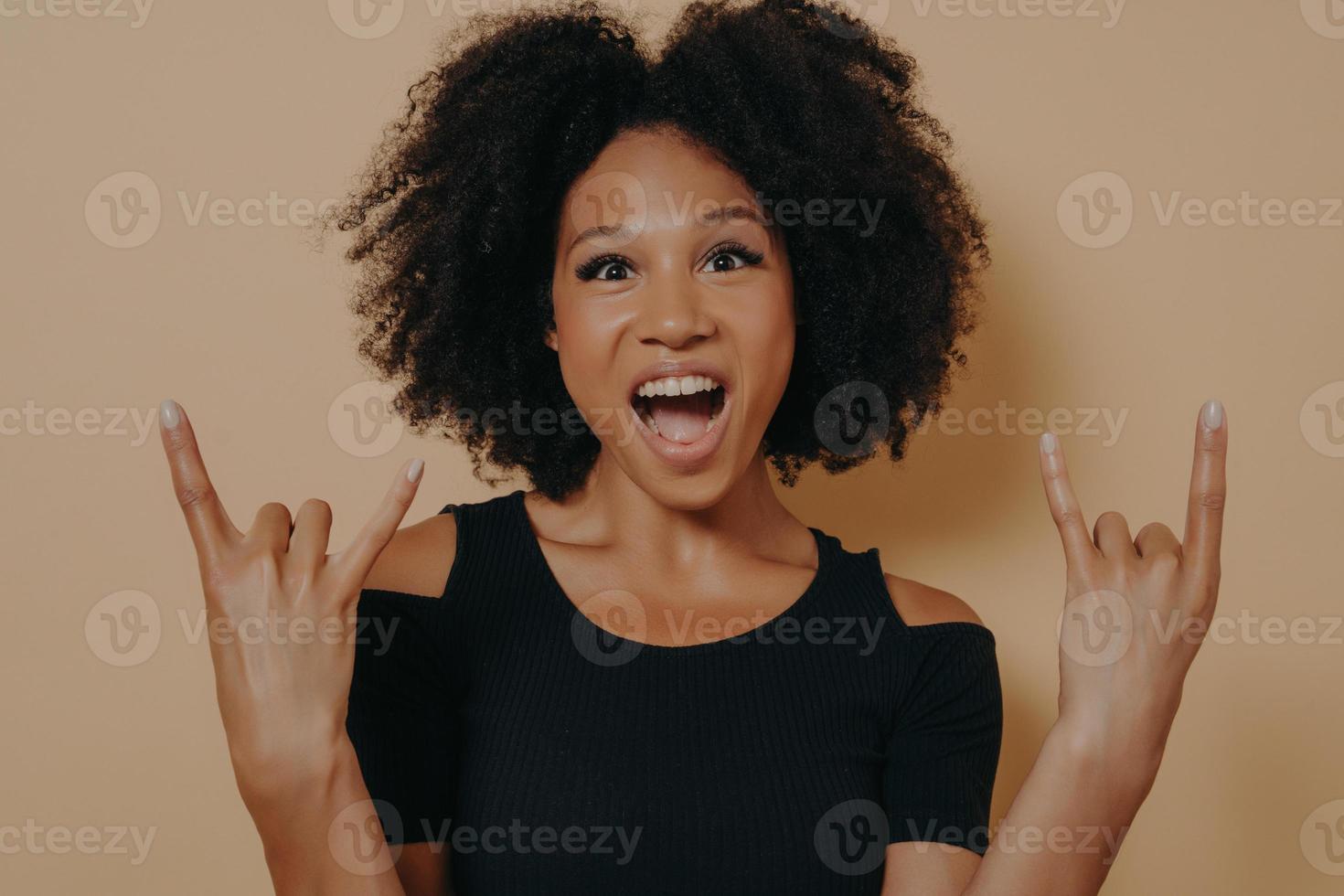 mujer joven con camiseta negra gritando con expresión facial loca haciendo símbolo de rock-n-roll foto