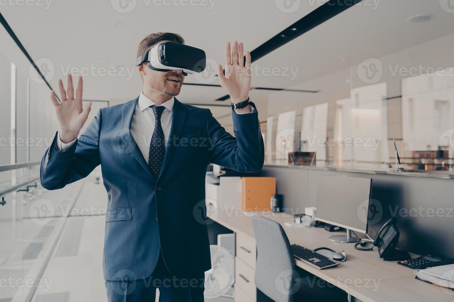 Businessman in virtual reality glasses standing near working desk in office photo