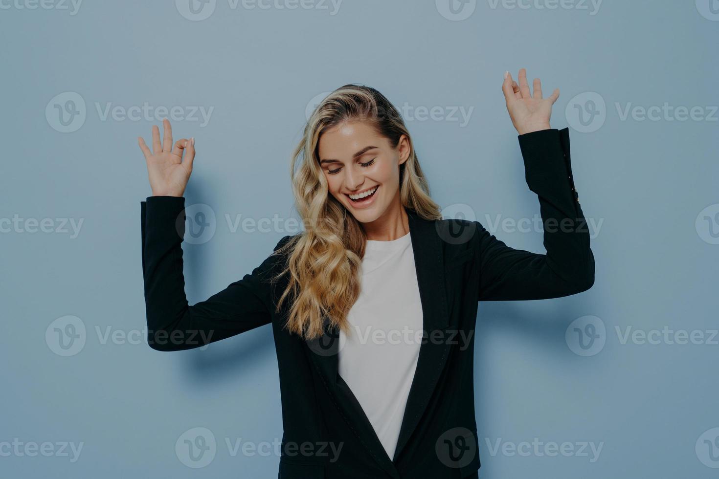 mujer feliz despreocupada con el pelo teñido de rubio levantando los brazos y bailando con los ojos cerrados y una sonrisa en la cara foto